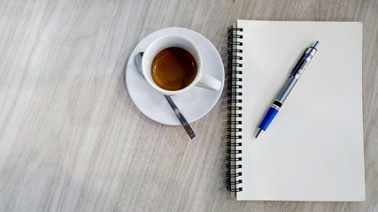 A Coffee cup and notebooks blank page with pen on wooden table with copy space backgrounds above