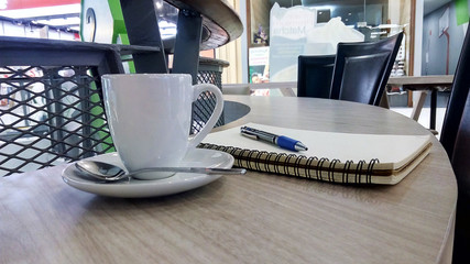 A white coffee cup and notebooks and pen on coffee bar table