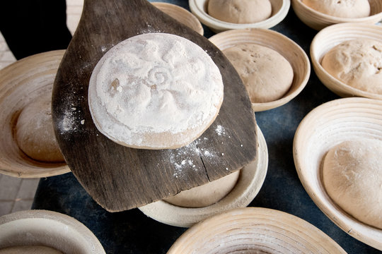handgemachter Laib Bauernbrot auf Brotschieber &uuml;ber Brotlaiben in Brotk&ouml;rbchen