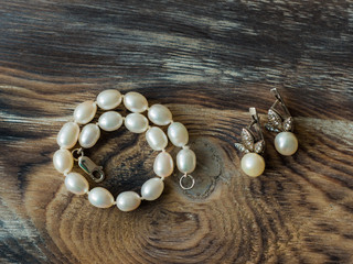 Top view on Elegant set of pearl braclet and earrings on wooden background. Close up