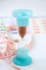 Hourglass, White centimeter and the calendar on a light background