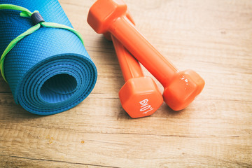 Yoga mat and dumbbells on wooden background