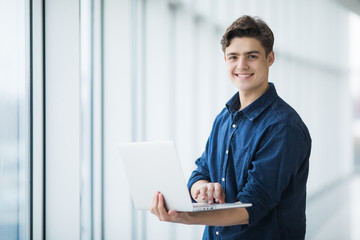 Handsome young man man holding a laptop in hall