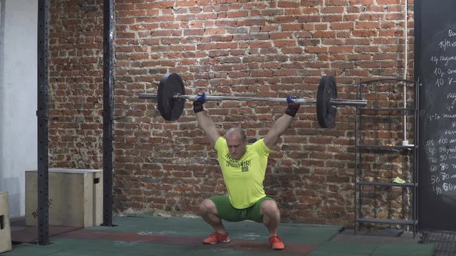 Man athlete doing squats with a barbell over his head in the gym