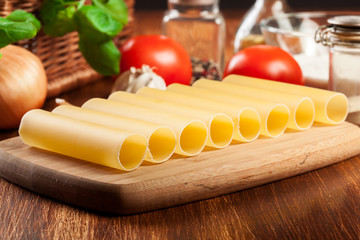 Uncooked cannelloni pasta on cutting board and ingredients