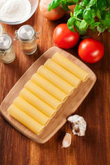 Uncooked cannelloni pasta on cutting board and ingredients