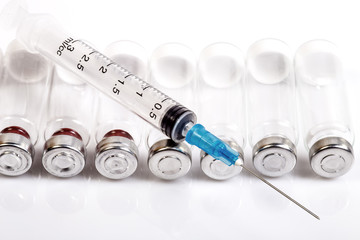 Vials with humane dry hormone lying in a row. Medical transparent syringe with needle without cap lying diagonally on the ampules. Forbidden doping for sportsmen and bodybuilders. Macro image. 