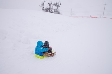 Fototapeta na wymiar 雪の降る中そりで遊ぶ子ども