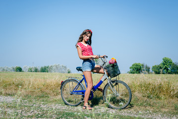 Fototapeta premium Young pinup woman cycling in fields under bright blue summer sky copy space image