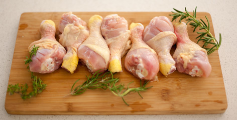 Chicken drumsticks on a cutting board with fresh rosemary and thyme. 
