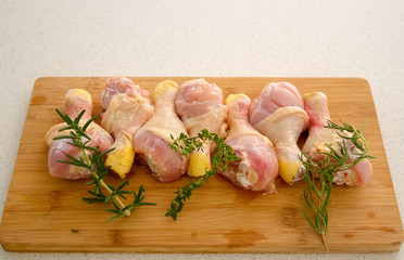 Chicken drumsticks on a cutting board with fresh rosemary and thyme.