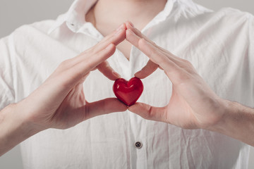 man in white shirt holds in hands red heart on gray background. 