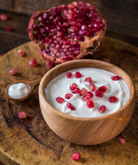 White yogurt with pomegranates in wooden bowl on rustic table.