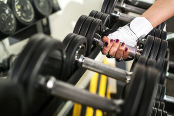 Fototapeta na wymiar Hand of a female hand taking a dumbbell out of set of black weights.