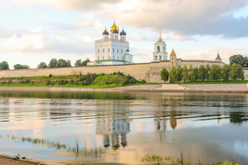 Fototapeta na wymiar Ancient old fortress on the river bank bright clouds sky July, Russia - Pskov Kremlin wall, Trinity Cathedral, Bell Tower and Dovmontova (Smerdya) tower at the sunset. View from the Velikaya river