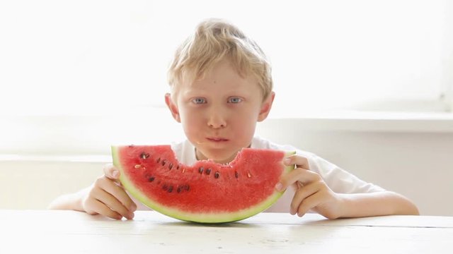 Little boy eats big red slice of a watermelon