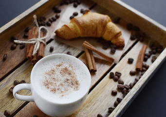 White cup of cappuccino and croissant on the wooden tray