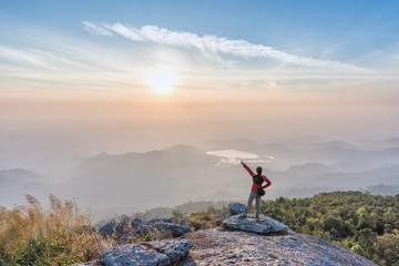 Woman successful climbing standing on the cliff and pointing to the sun.