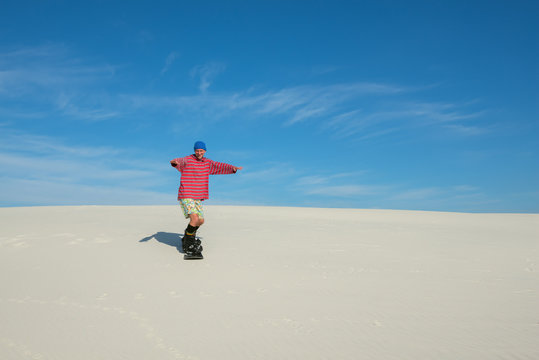 Joyful man slides down on a snowboard on the sand dune