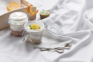 Obraz na płótnie Canvas Healthy breakfast of muesli with yogurt and fruit in a glass jar in a tray in bed