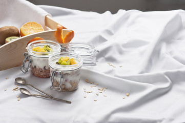 Healthy breakfast of muesli with yogurt and fruit in a glass jar in a tray in bed