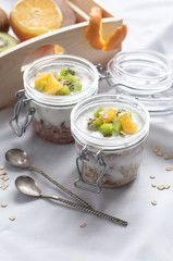 Healthy breakfast of muesli with yogurt and fruit in a glass jar in a tray in bed