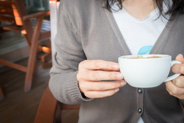 Woman's hand holding a cup of redolent cappuccino coffee.