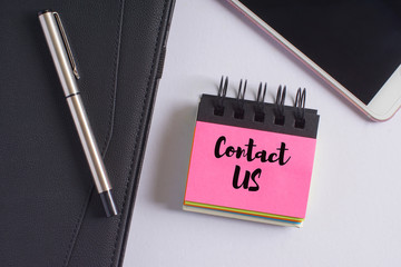 "Contact us" words on pink sticky notes with fountain pen, diary and smartphone on white background - business and finance concept