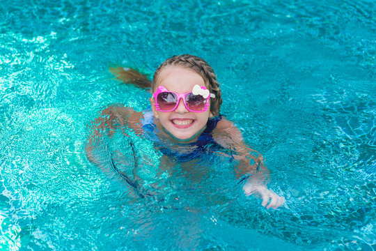 cheerful girl child resting in pool wearing sunglasses