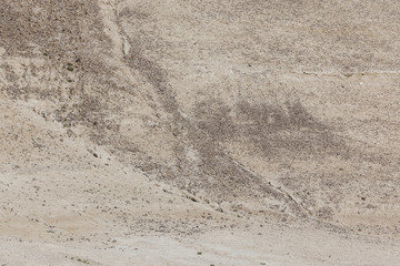 Arid dry cracked yellowish soil slope with small stones and little vegetation
