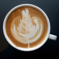 Top view of a mug of latte art coffee on black background.
