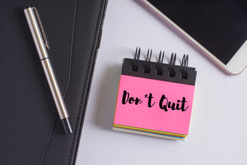 "Don't quit" words on pink sticky notes with fountain pen, diary and smartphone on white background - business and finance concept