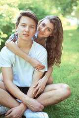 Portrait sweet smiling young couple teenagers sitting on the grass in summer day