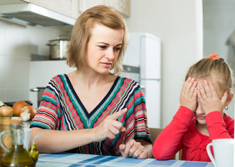 woman lecturing small female child in the kitchen