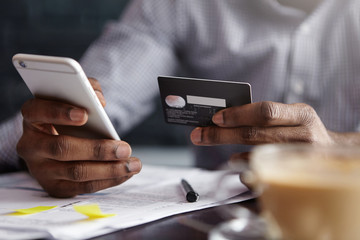Cropped shot of African-American businessman paying with credit card online making orders via...