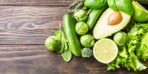 Background with assorted green vegetables, salad, avocado, cucumber, lime and Brussels sprouts on wooden table top. Healthy food concept with copy space.