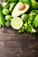 Background with assorted green vegetables, salad, avocado, cucumber, lime and Brussels sprouts on wooden table top. Healthy food concept with copy space.