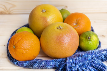 orange fruits,grapefruits and limes wrapped in a  scarf on a wooden background.Winter fruit diet