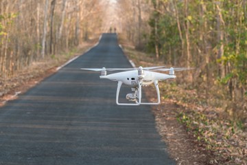 Quadrocopter drone flying on the tarmac road with trees background..
drone flies with mounted digital camera for video and photo productions. 