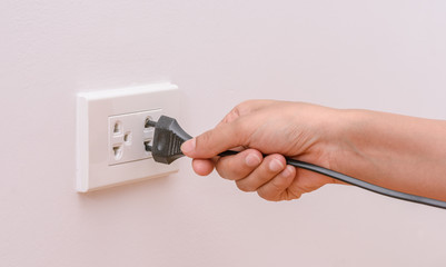 Female hand trying to plugging in appliance to electrical outlet in wall