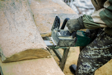 Man in camouflage thick wood saws chainsaw. Flying dust from the drink