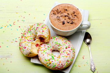 Cup of coffee and tasty donuts with icing and chocolate on green wooden background, copy space