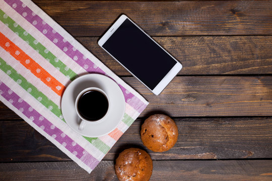Coffee in white cup with two cupcakes on mobile phone
