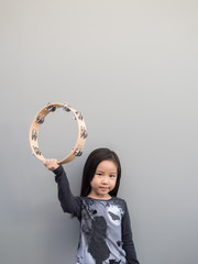 Little asian child play the tambourine, gray background