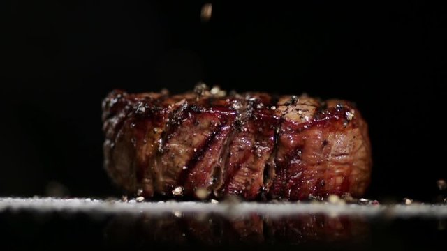 SLOW MOTION FOOD: large grains of pepper fall on juicy grilled filet mignon close up