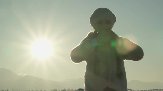 Child girl hands make heart at sunset in mountains in sunny winter day