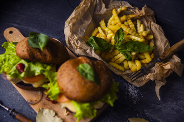Fast food on the table: burger with beef or pork, or chicken and vegetables, French fries with tomato sauce, basil leaves
