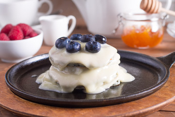 Breakfast, pancakes with maple syrup and fresh berries in a cast iron skillet. Wooden background. Selective focus