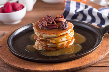 Breakfast, pancakes with maple syrup and nuts in a cast iron skillet. Wooden background. Selective focus
