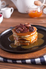 Breakfast, pancakes with maple syrup and nuts in a cast iron skillet. Wooden background. Selective focus